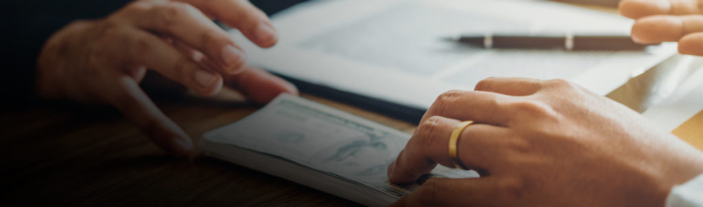 Hand slides money across a desk during the course of securities fraud.