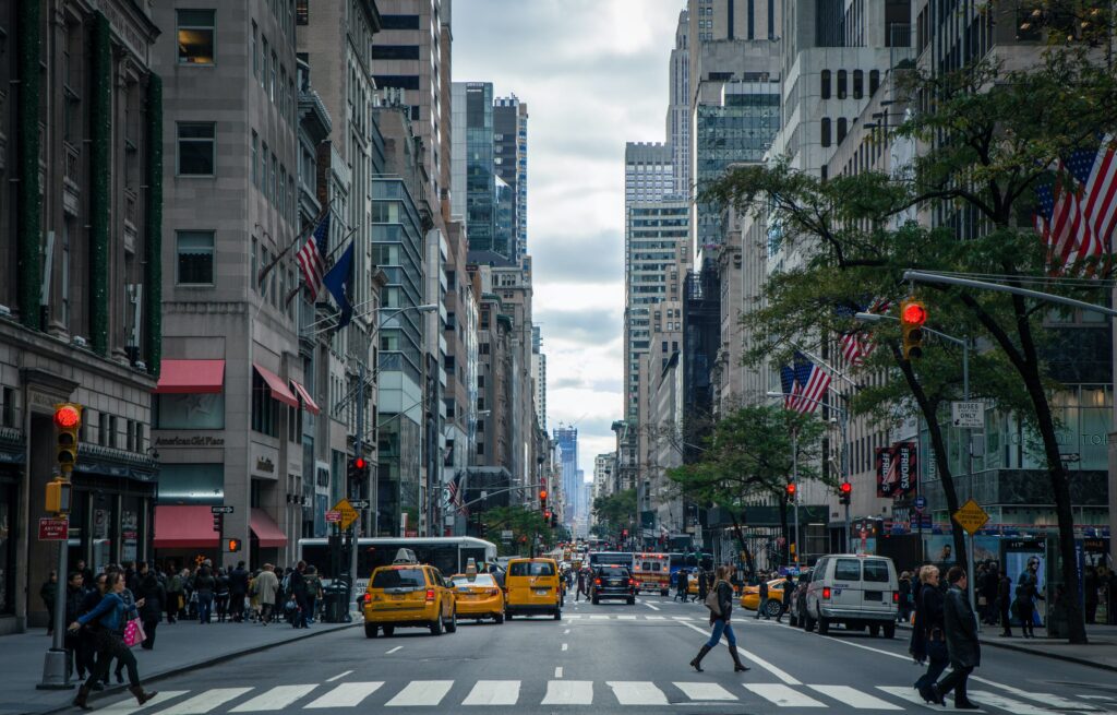 New York City street lined with skyscrapers and taxi cabs. A pedestrian is crossing thre street. 